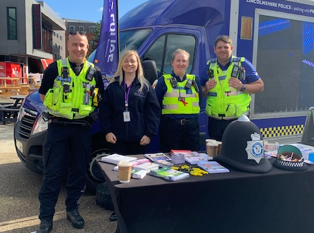 The Safer Together Coordinator standing in the sunshine with Lincolnshire Police. A stand displays police uniform and various awareness leaflets